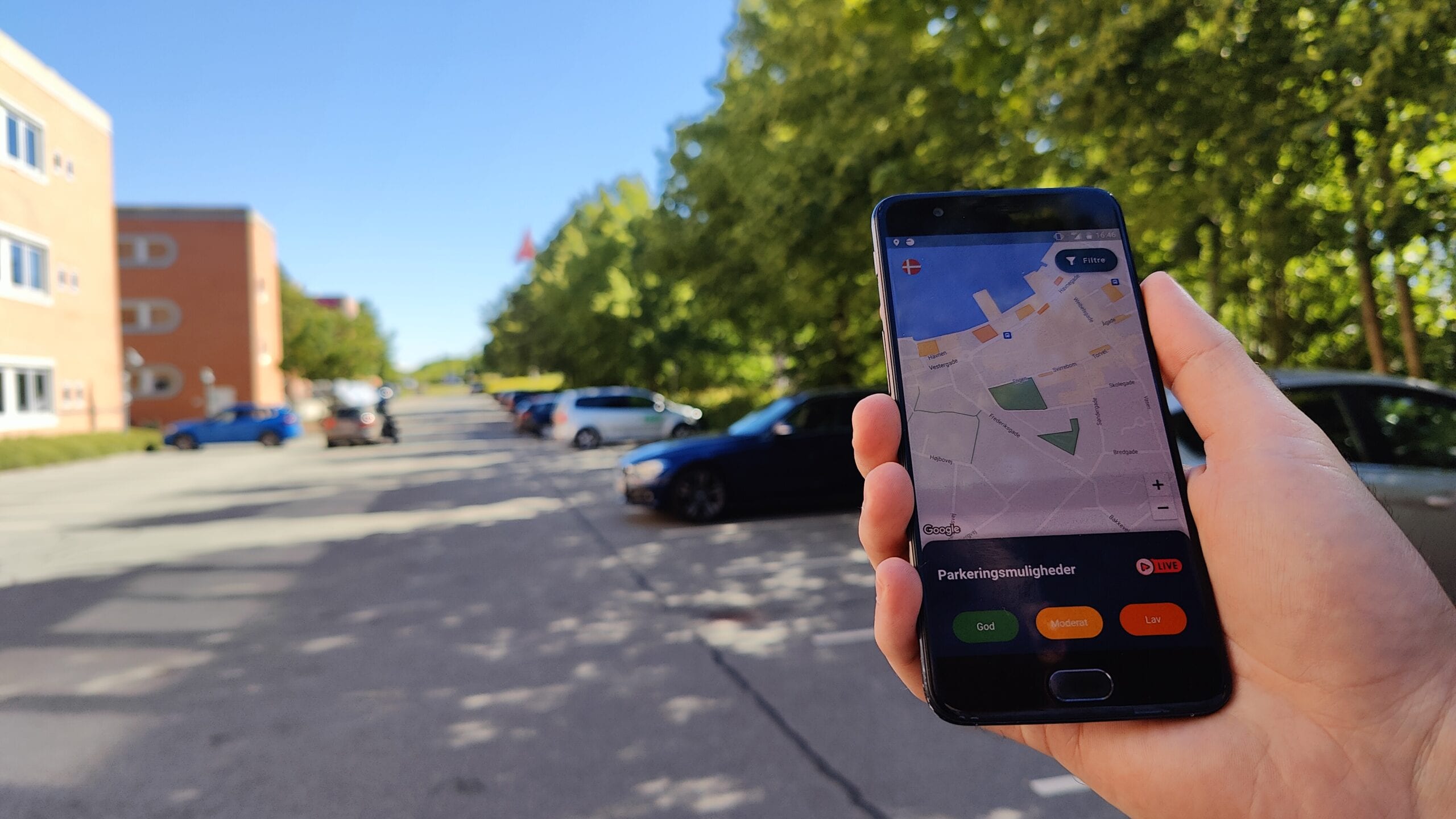 Hånd med telefon og parkeringsapp foran en parkeringsplads
